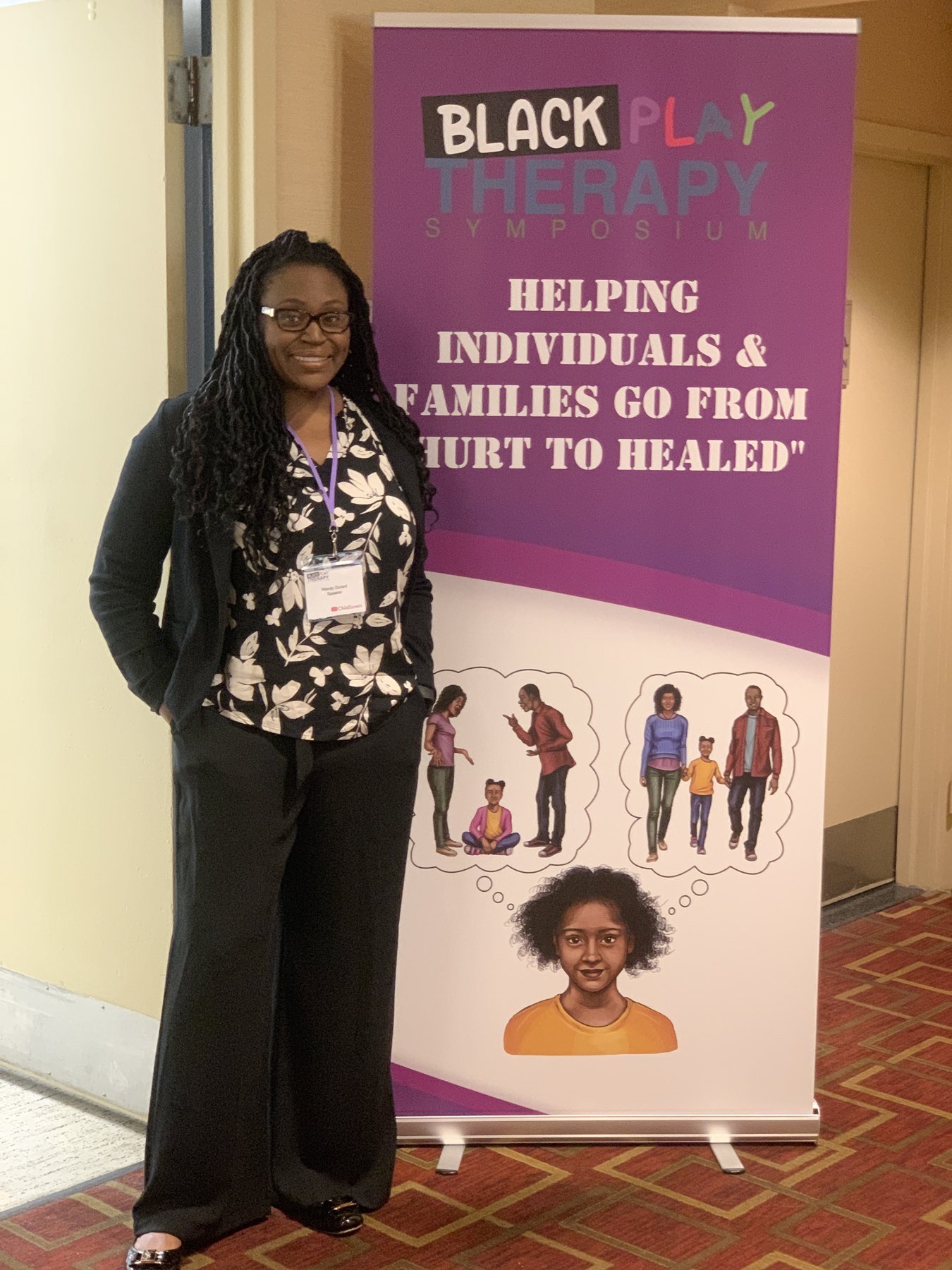 Wendy Durant standing beside a Black Play Therapy Symposium presentation banner